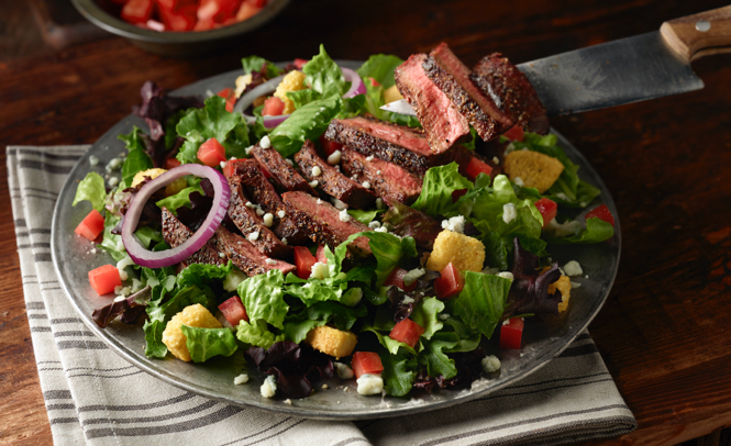 Large salad on a plate with sliced steak on top