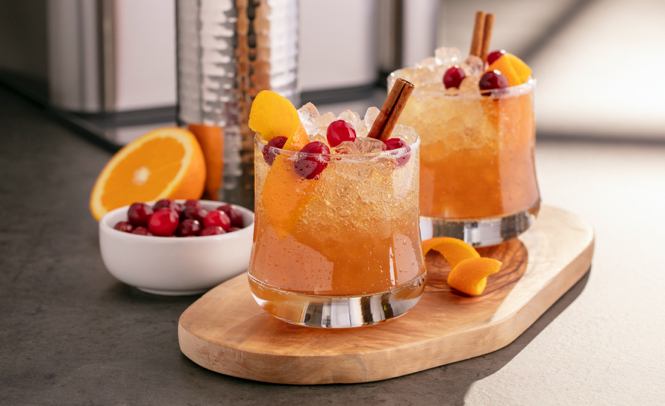 Two orange colored cocktails with fruit and cinnamon sticks poking out